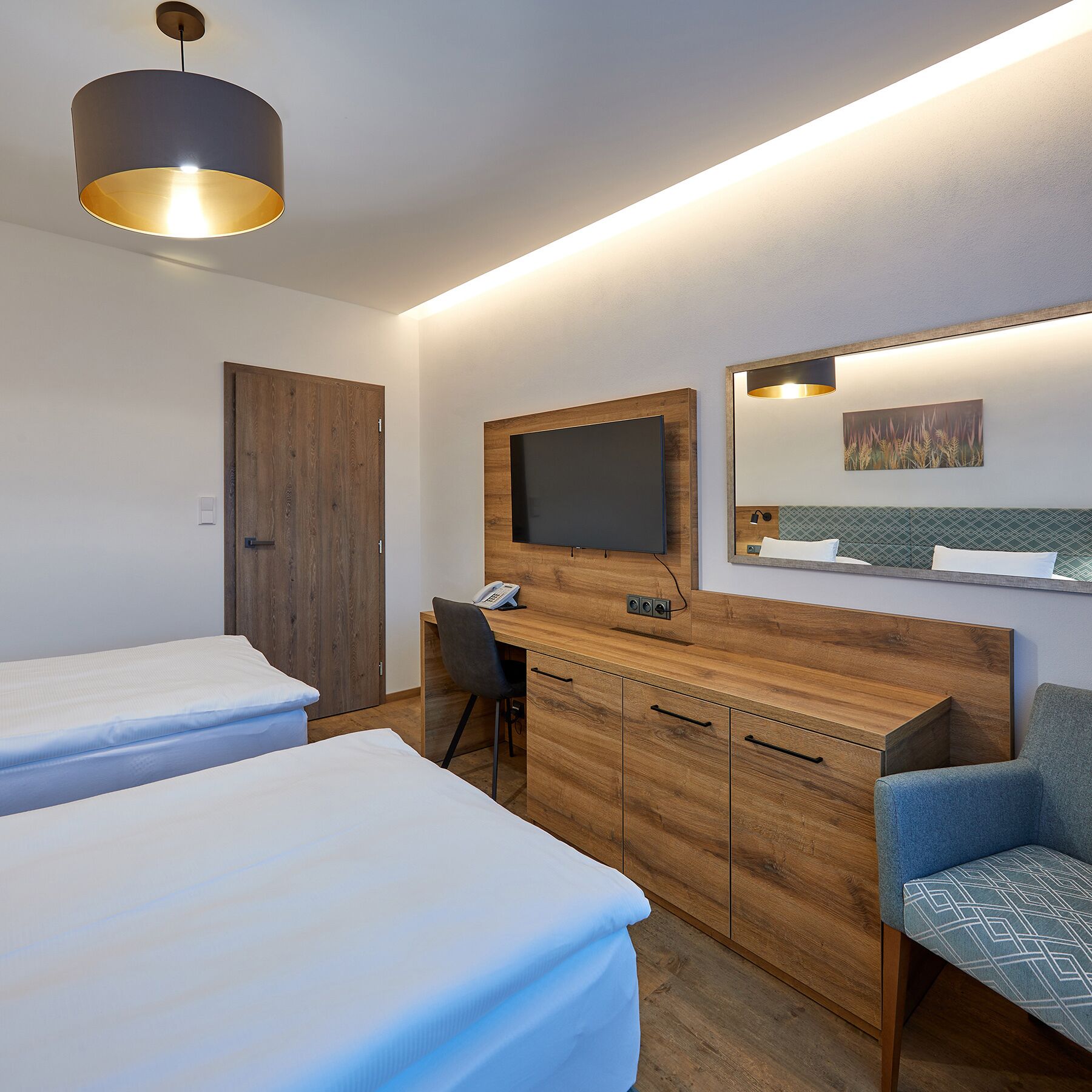 A hotel room with two beds, a desk, a chair, a TV, and a mirror.
