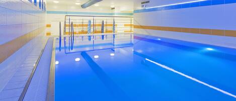 Una piscina con tonalidades azules, paredes enlosadas y sistema de ventilación.
