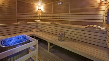 A sauna with wooden benches, a bench heater, and a stone basin.