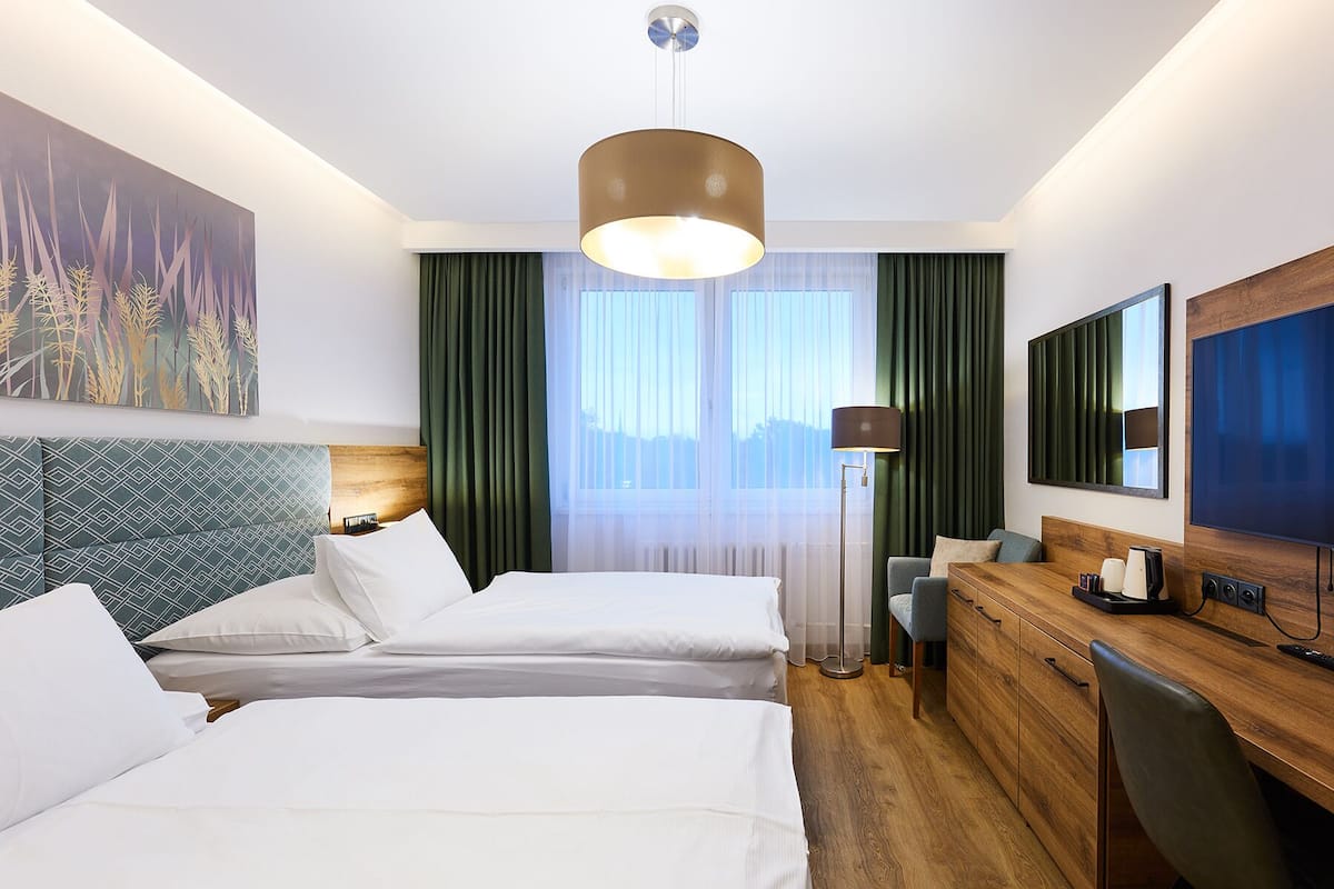 Een hotelkamer met twee bedden, een bureau, een stoel, een televisie en een groot raam met gordijnen.