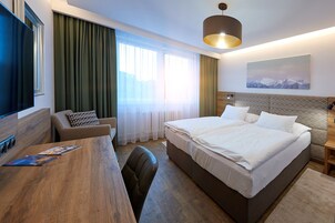 Una habitación de hotel con una cama grande, un escritorio con silla, televisor y ventana con cortinas.