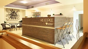 A reception area with a wooden reception desk, wicker chairs, and a modern ceiling design. - Central Park Flora (Olomouc)