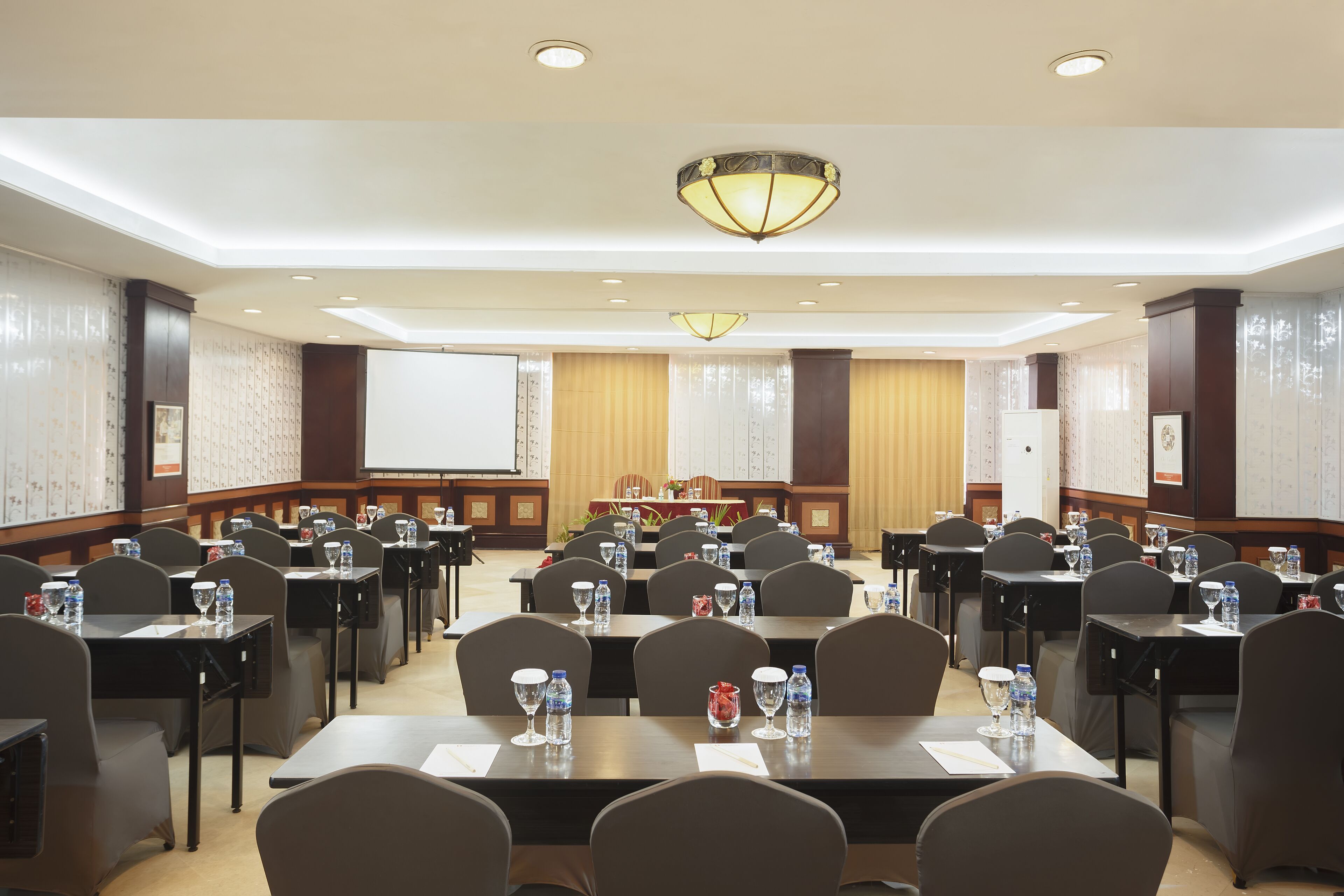 A conference room with tables, chairs, and a projector screen.