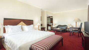 Une chambre d’hôtel avec un grand lit, un bureau, une chaise, un téléviseur et un sol recouvert d’une moquette rouge.