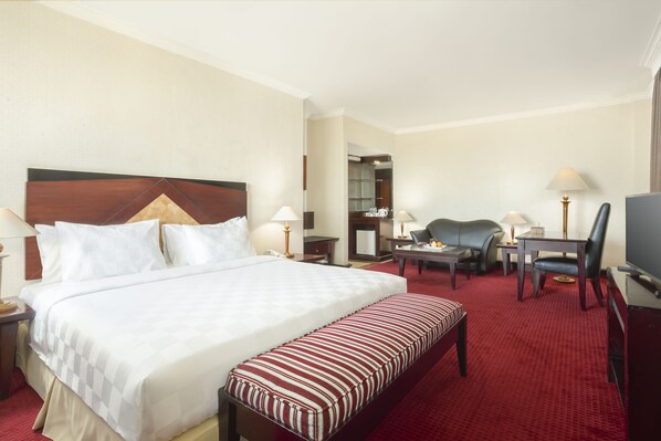 A hotel room with a large bed, a desk, a chair, a television, and a red carpeted floor. - Swiss-Belhotel Tarakan (Tarakan)