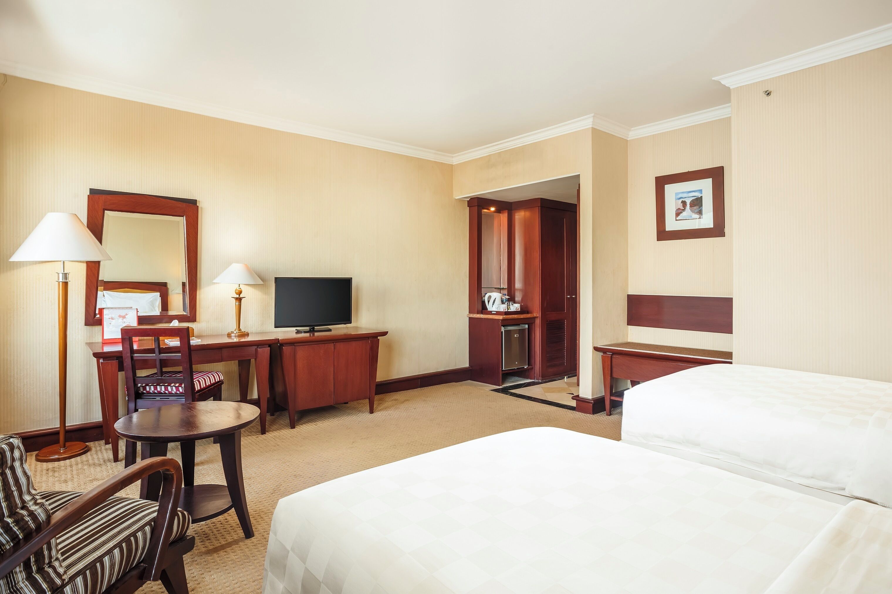Habitación de hotel con cama, escritorio, silla, televisor y una mesita de noche con lámpara.