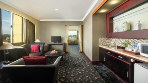A hotel room with a sofa, a small table with a lamp, a TV, a kitchen area with a microwave, and a view of the outdoors. - Swiss-Belhotel Tarakan (Tarakan)