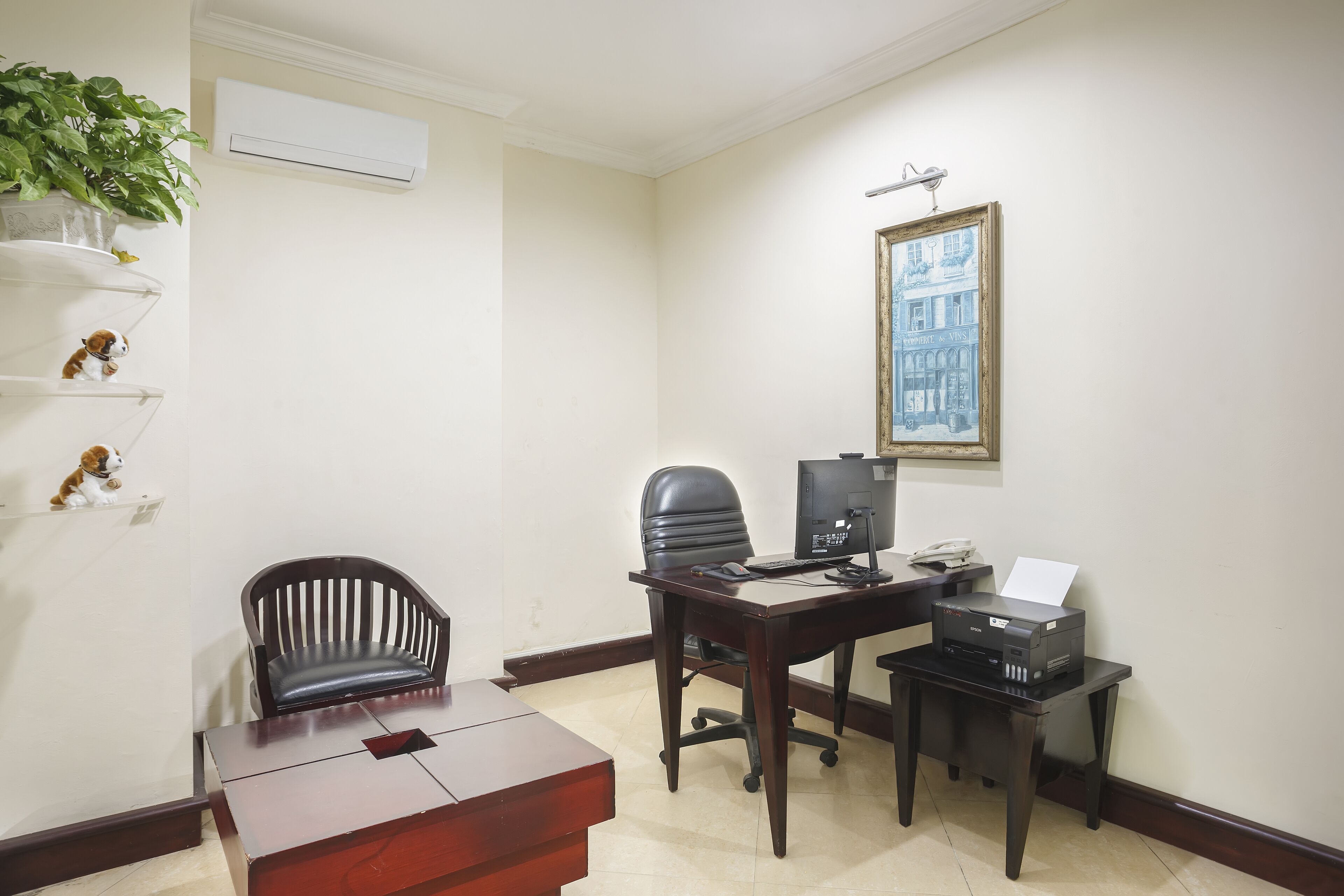 Un petit bureau avec un bureau, deux chaises, une imprimante, un ordinateur et un tableau encadré accroché au mur.