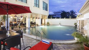 A hotel pool area with lounge chairs, a red umbrella, and potted plants. - Swiss-Belhotel Tarakan (Tarakan)