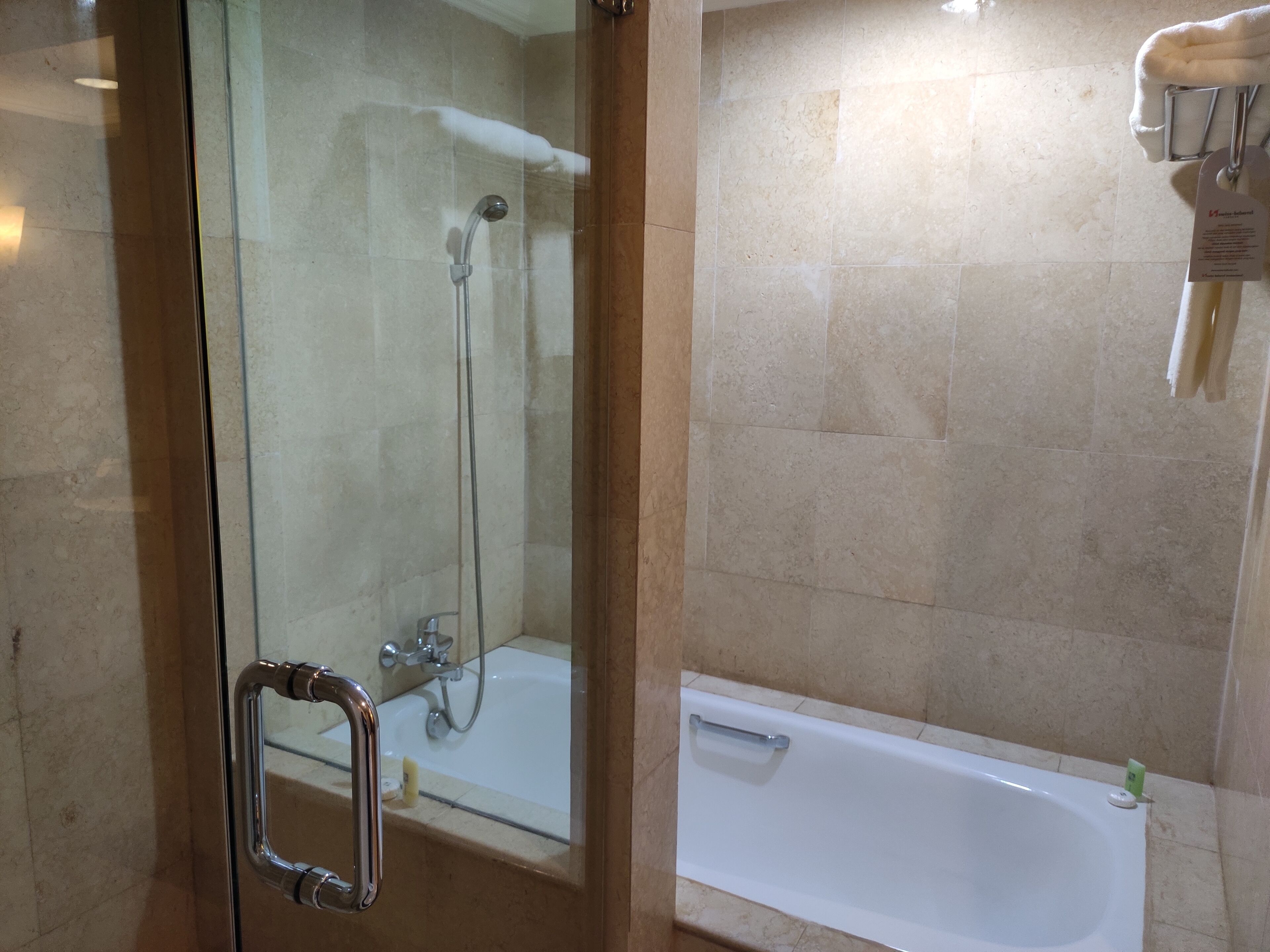 Een badkamer met een douche in een glazen cabine, een witte badkuip en beigekleurige betegelde wanden.