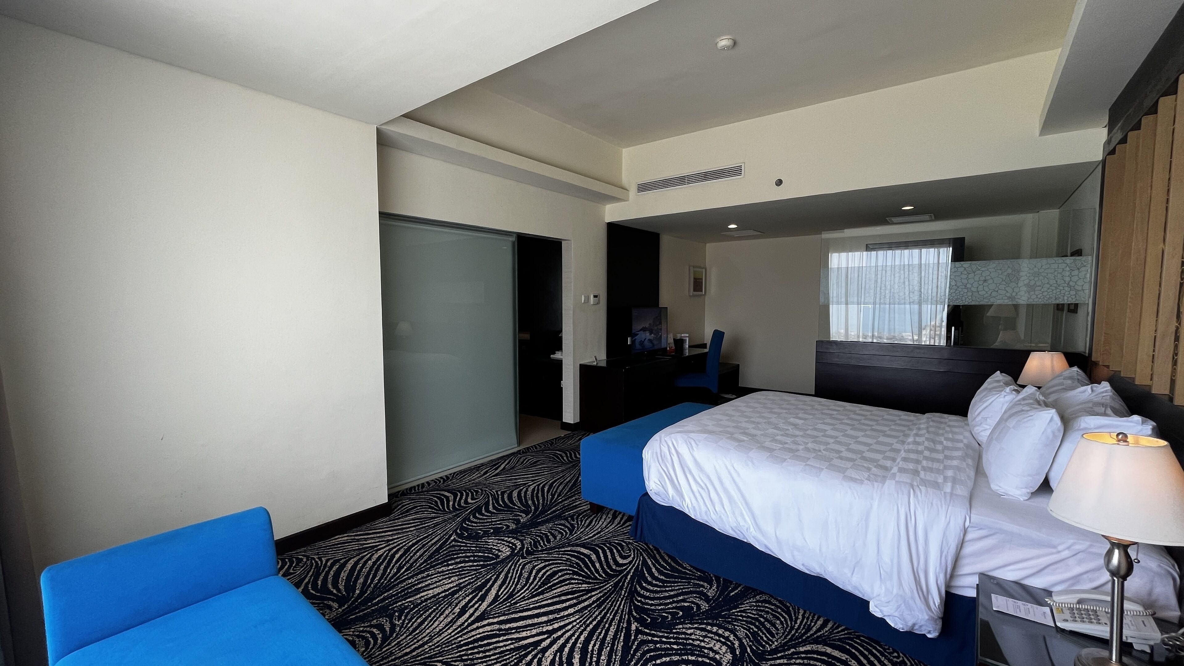 A hotel room with a large bed, a desk, a chair, and a window with a view.