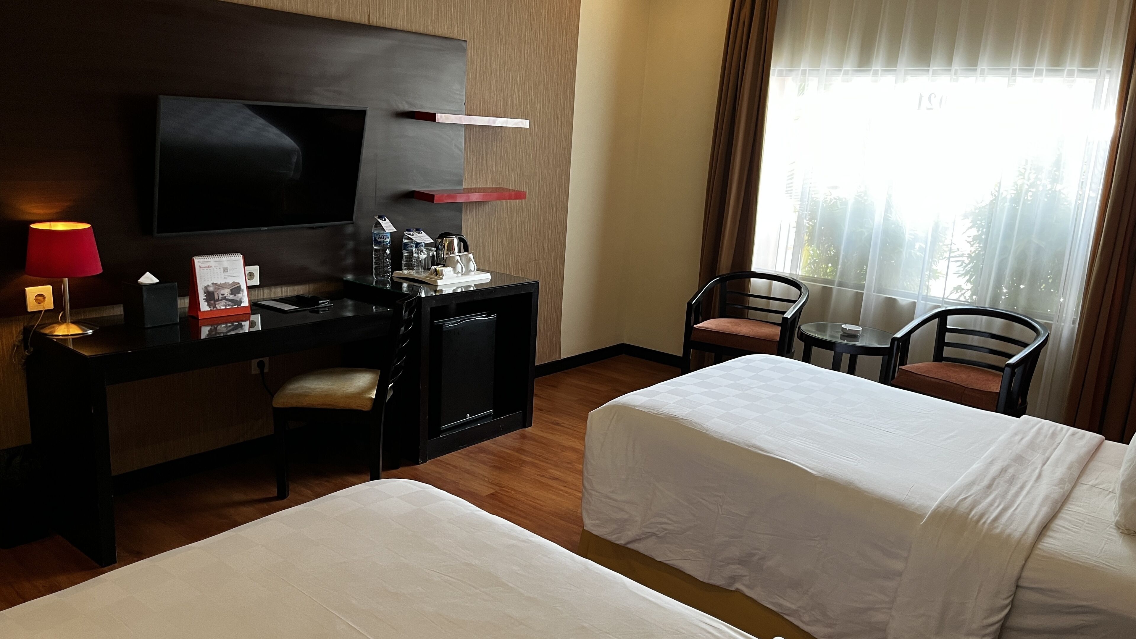 A hotel room with two beds, a desk with a TV, a small table, and chairs.