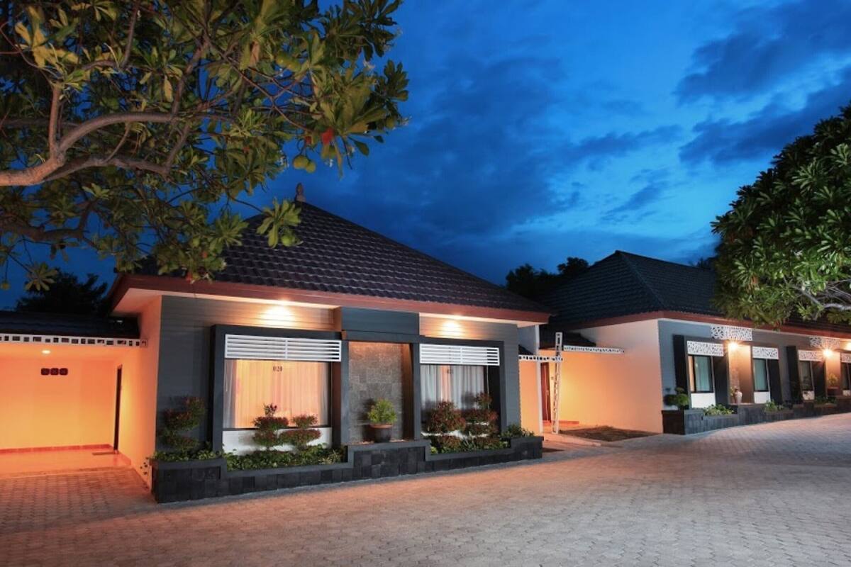 A modern hotel with a tiled roof, large windows with blinds, and a paved driveway.