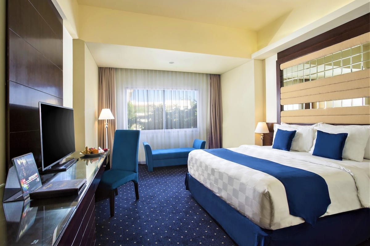 A hotel room with a bed, a desk with a TV, a chair, and a window with curtains.