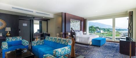 Habitación de hotel con una cama grande, un sofá azul, una mesita de centro y vistas a las montañas.