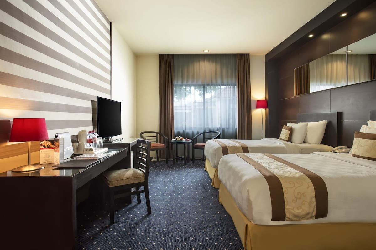 A hotel room with two beds, a desk with a computer, a chair, a small table, and a TV.