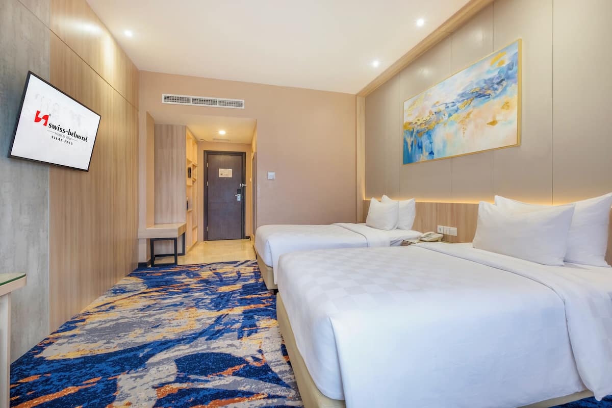A hotel room with two beds, a large abstract painting, and a sign for Swiss-Bellhotel.
