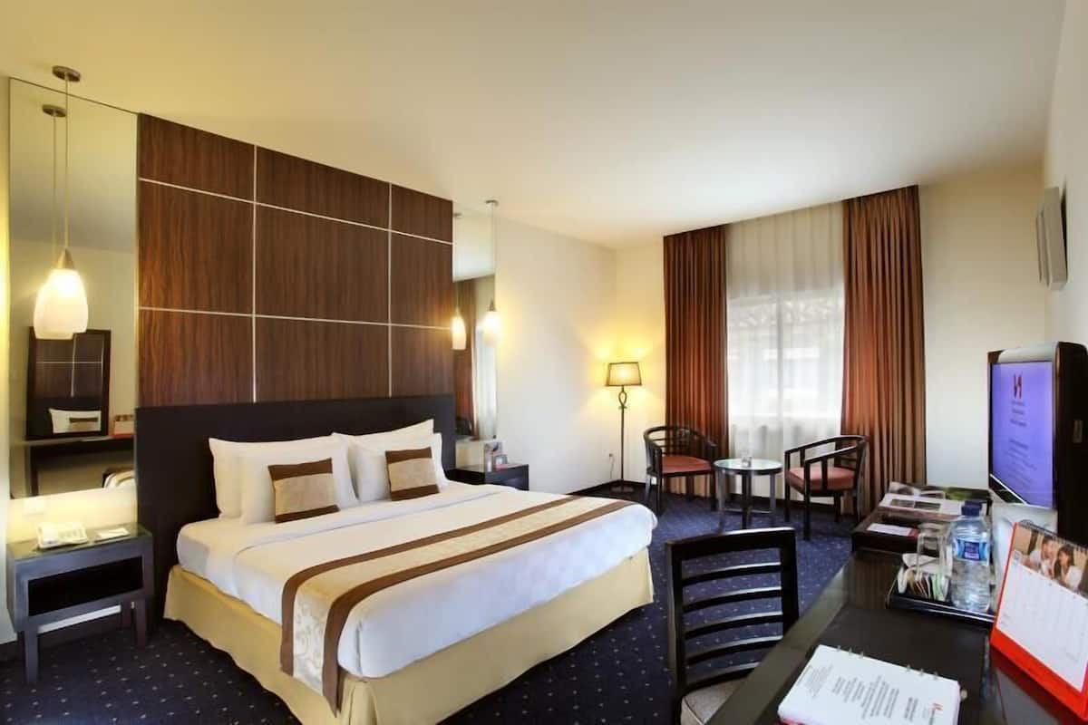 A hotel room with a bed, bedside tables, a desk with a chair, a TV, and a calendar.