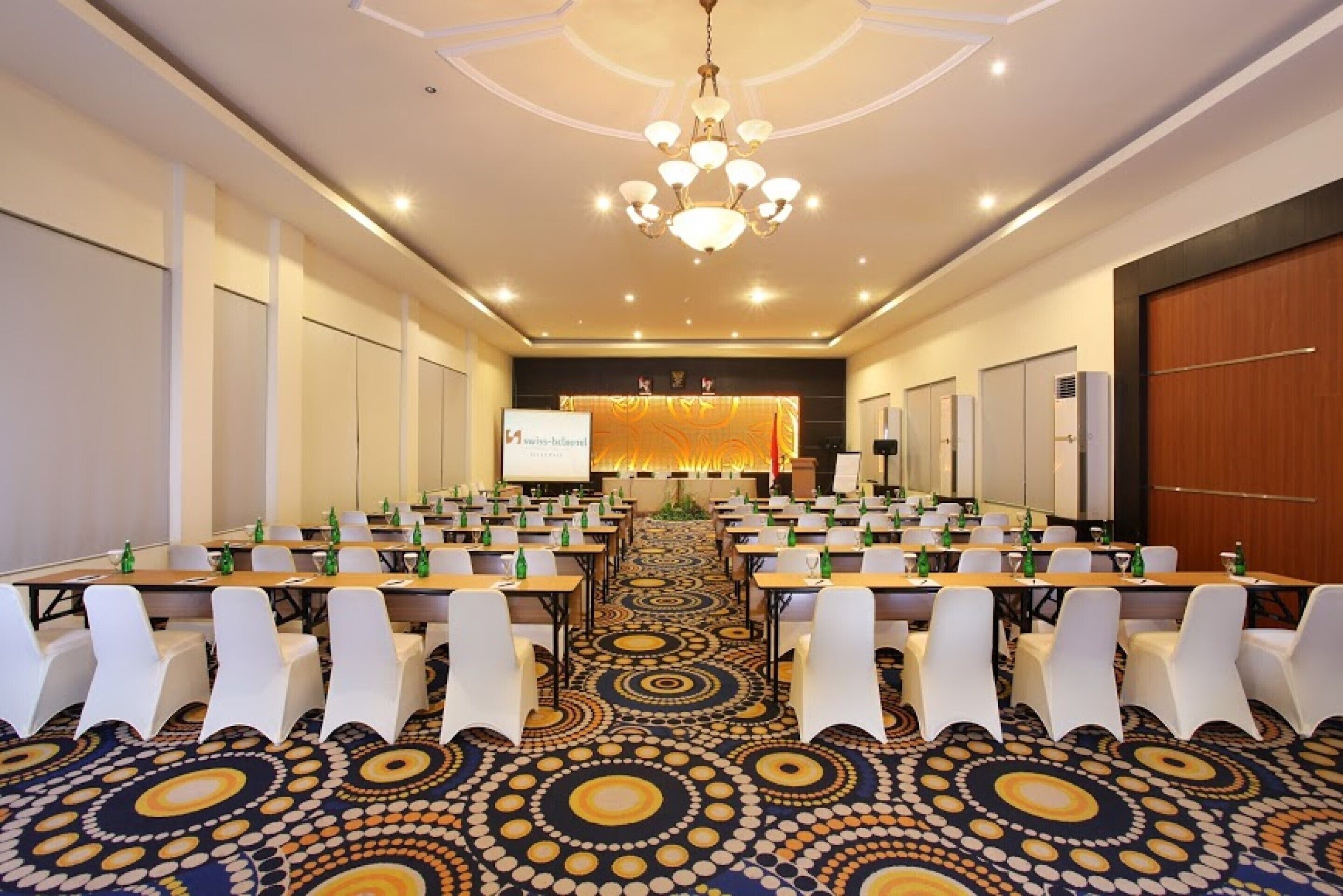 A conference room with a patterned carpet, white chairs, and a chandelier.