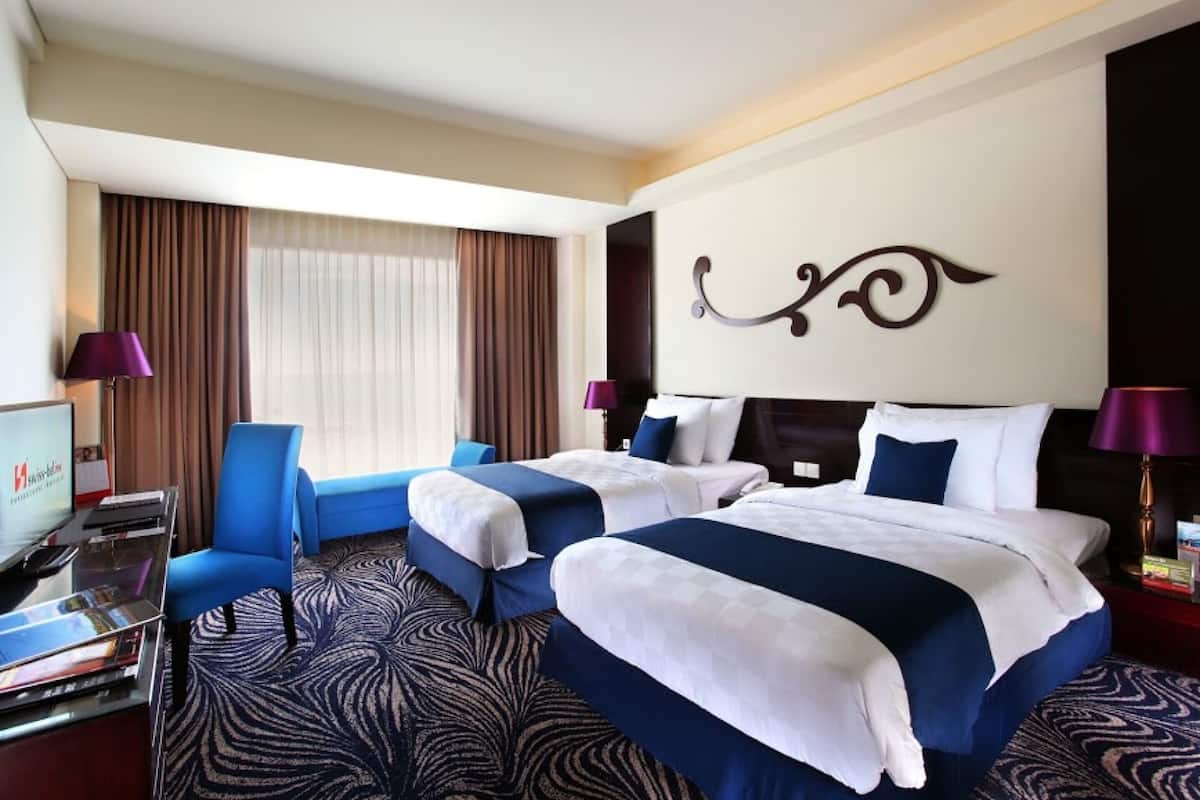 A hotel room with two beds, a desk with a computer, a chair, and a large window with curtains.