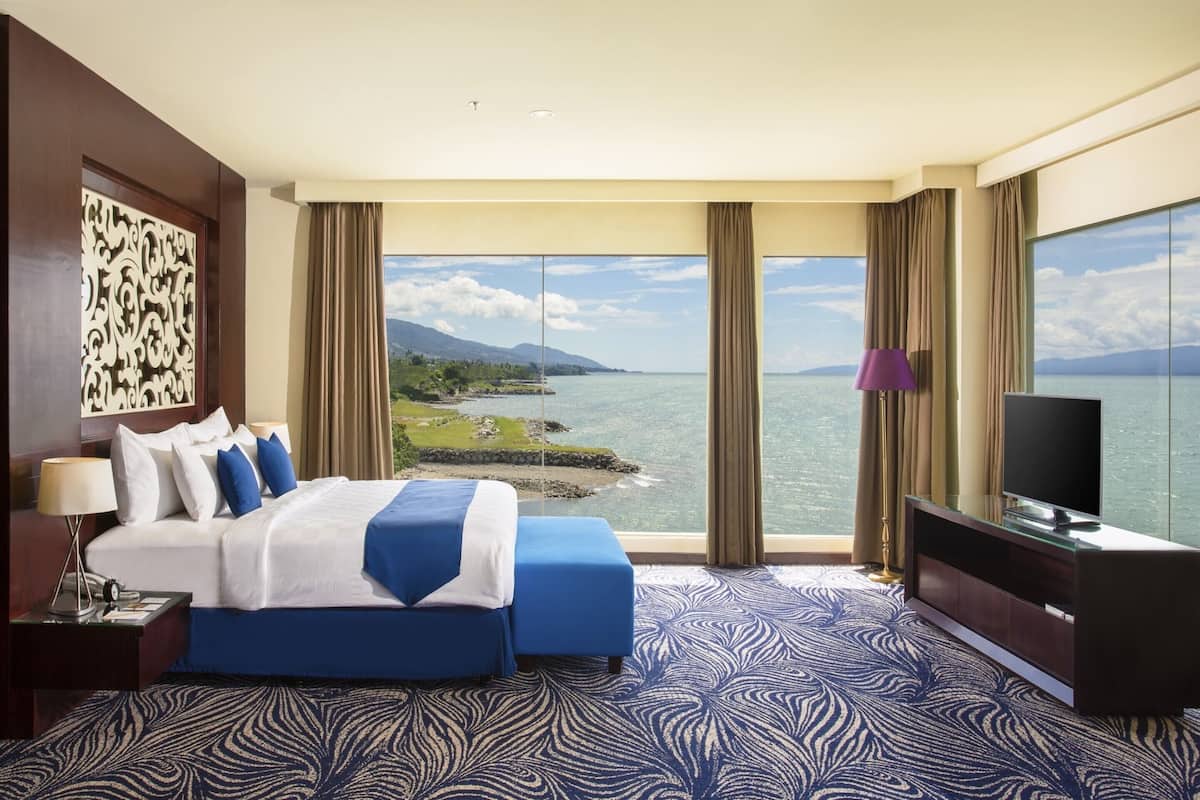 A hotel room with a large bed, a TV, and a view of the sea.