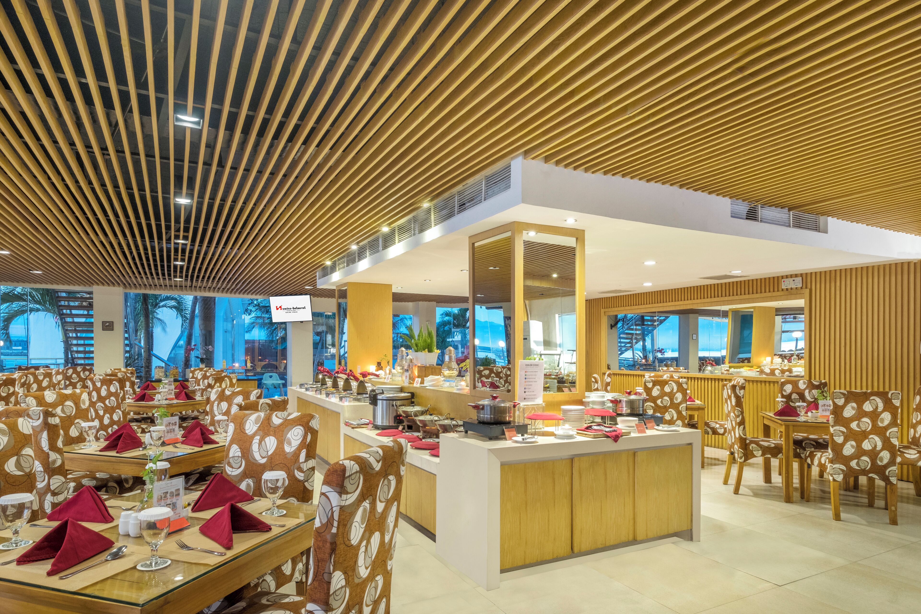 A restaurant with a modern design, featuring wooden panel ceilings, a central island with a buffet, and patterned chairs.