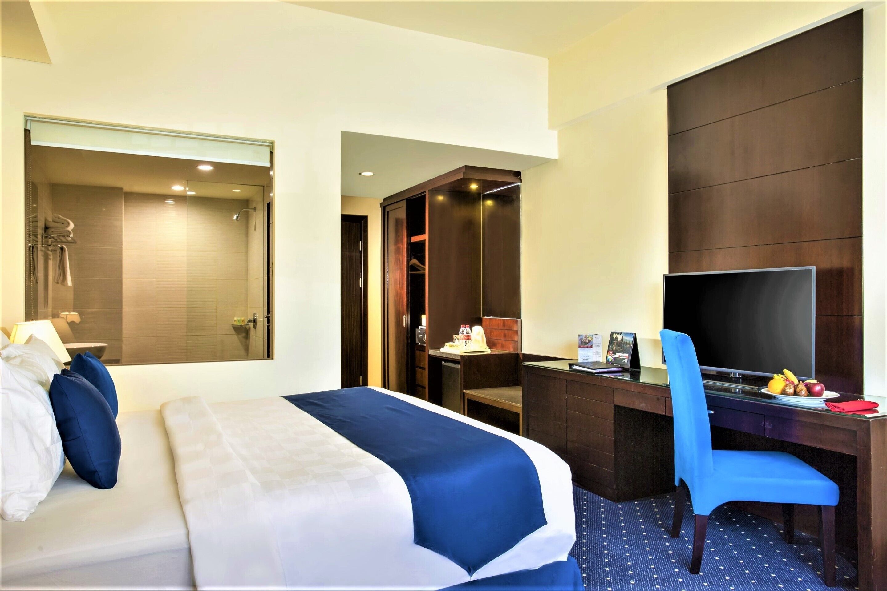 Habitación de hotel con cama, escritorio, silla, televisor y zona de ducha.