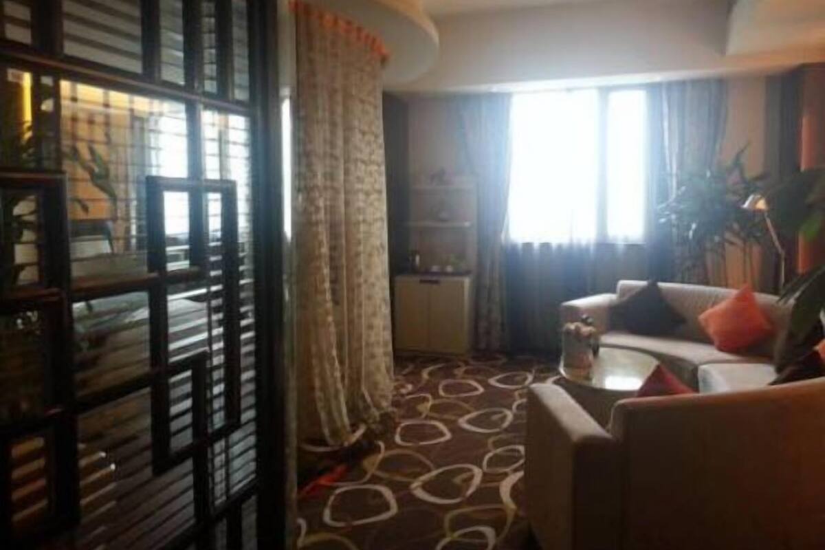 A hotel room with a patterned carpet, a sofa, a small table, and a window with curtains.