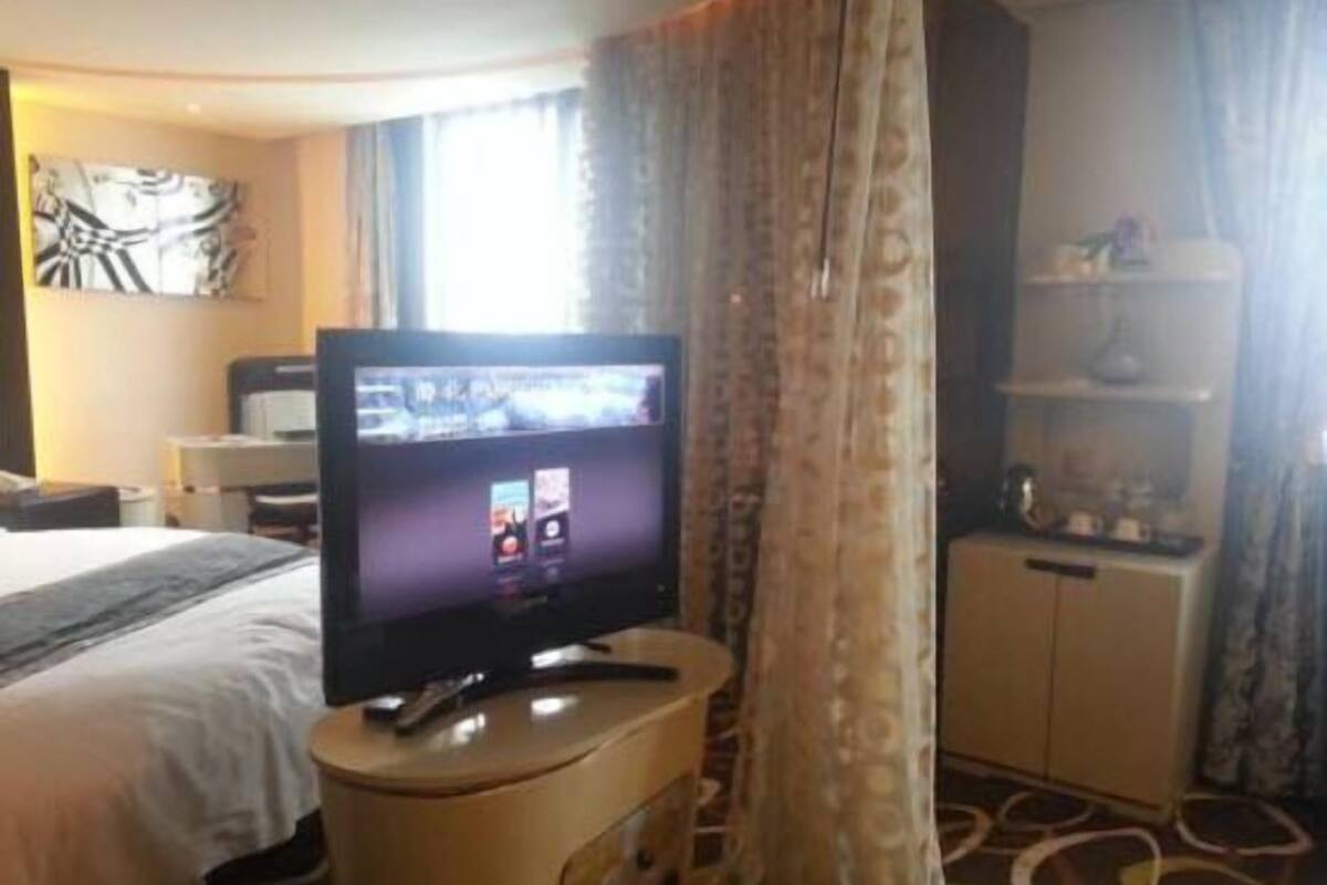 A hotel room with a bed, a television on a stand, a desk with a computer, and a cabinet.