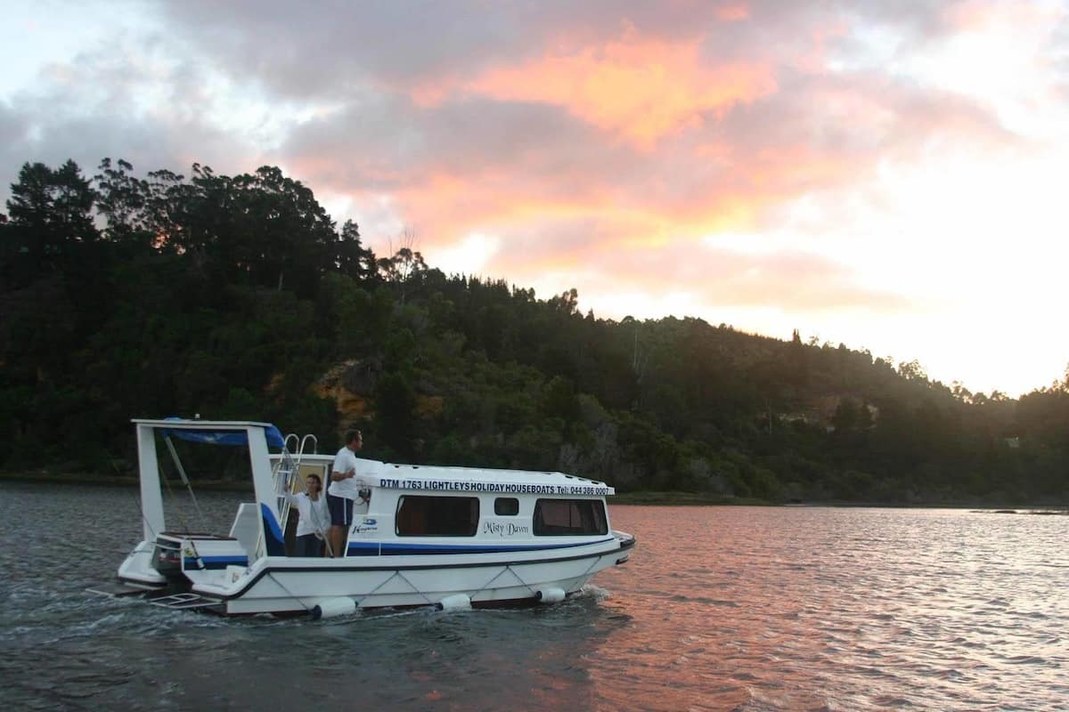 A boat with a cabin and a covered area, named "Misty Dawn," on a body of water with a forested hillside in the background.
