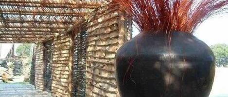Un jarrón oscuro con plumas rojas sobre una mesa en un espacio al aire libre cubierto, con un muro de piedra.