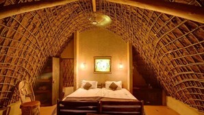 A room with a thatched roof, a bed with pillows, a framed picture on the wall, and a small table with a chair. - Hawane Resort (Motshane)