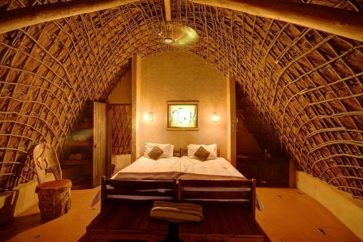 A room with a thatched roof, a bed with pillows, a framed picture on the wall, and a small table with a chair.