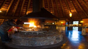 A restaurant with a stone fireplace, wooden ceiling, and a bar area. - Hawane Resort (Motshane)
