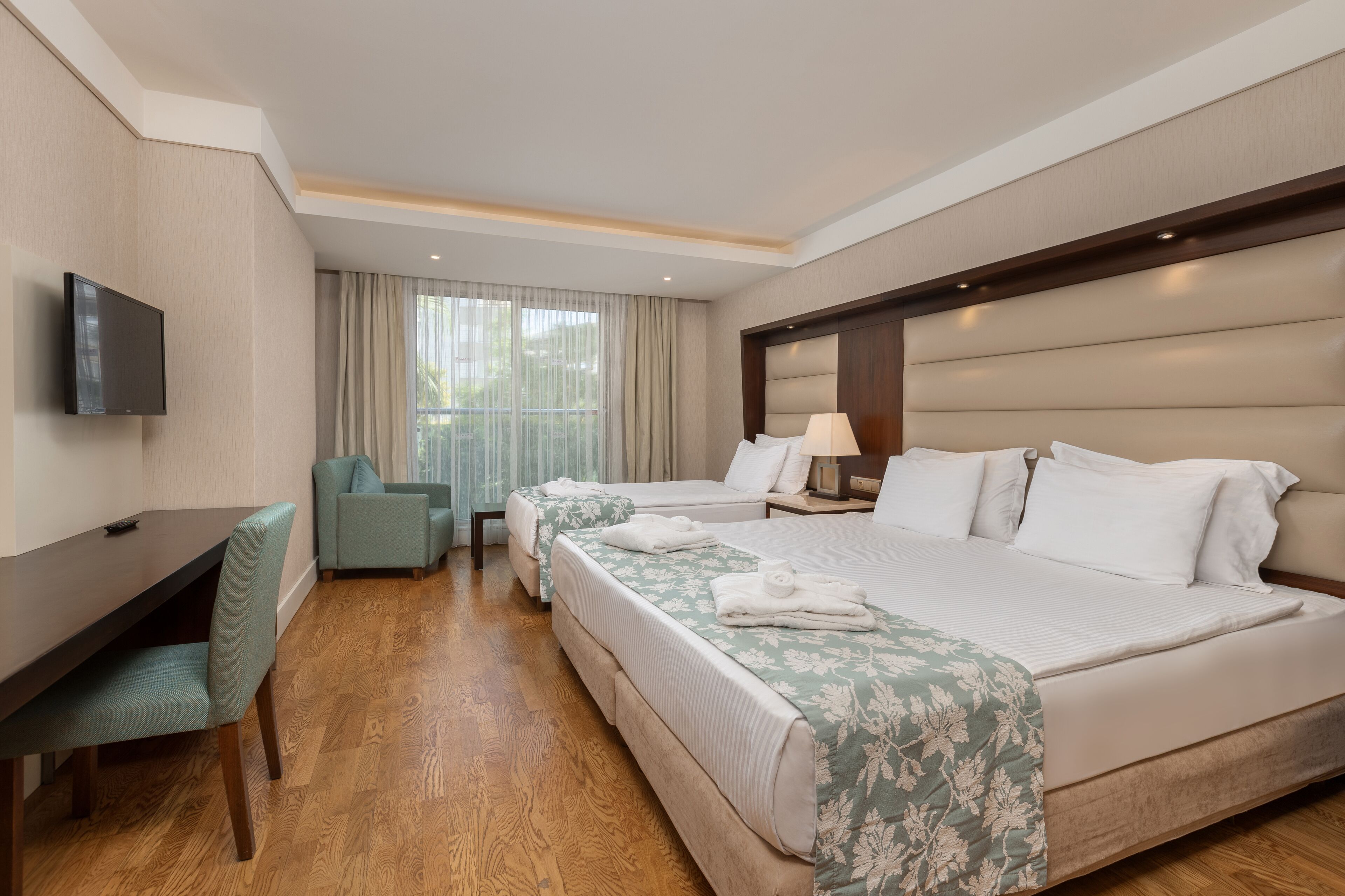 Une chambre d’hôtel avec deux lits, un bureau, une télévision et une fenêtre avec des rideaux.