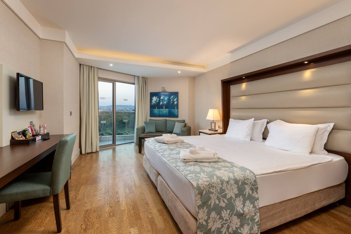 Une chambre d’hôtel avec un grand lit, un bureau, une chaise, une télévision, un tableau et une vue sur la ville.