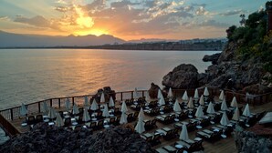 Un complejo turístico frente al mar, con vista al océano iluminado por el sol, sillas de descanso y sombrillas.