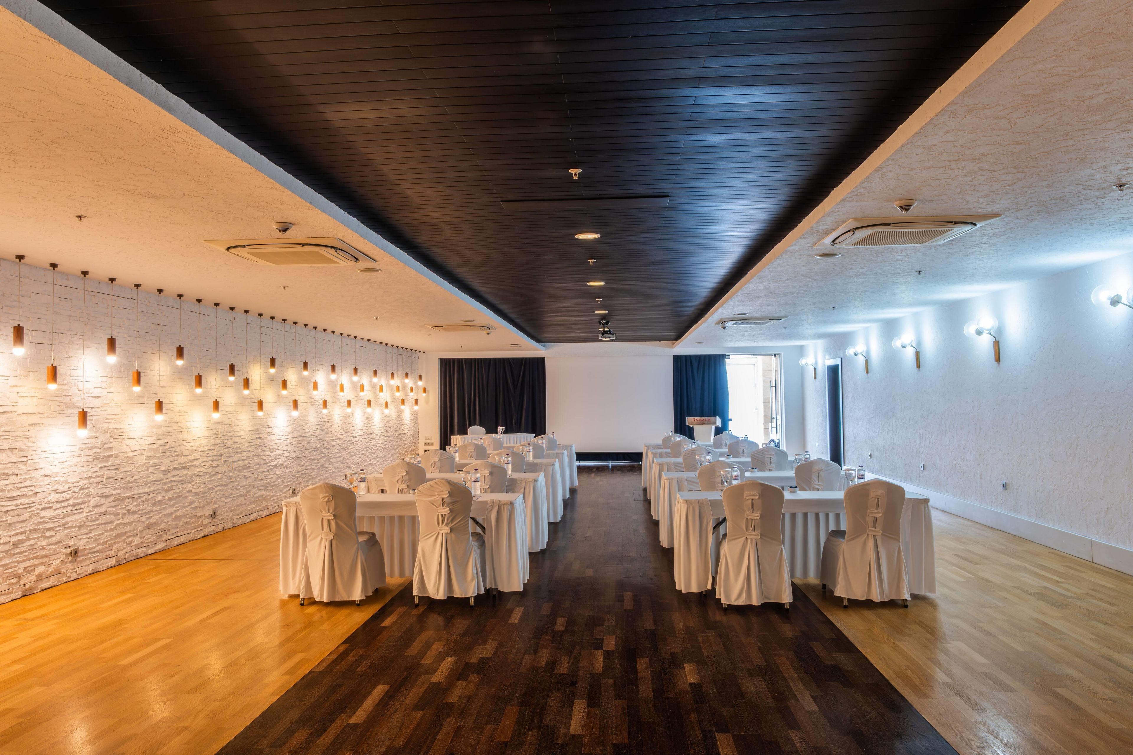 Een vergaderzaal met witte tafels en stoelen, houten vloeren en een bakstenen muur.