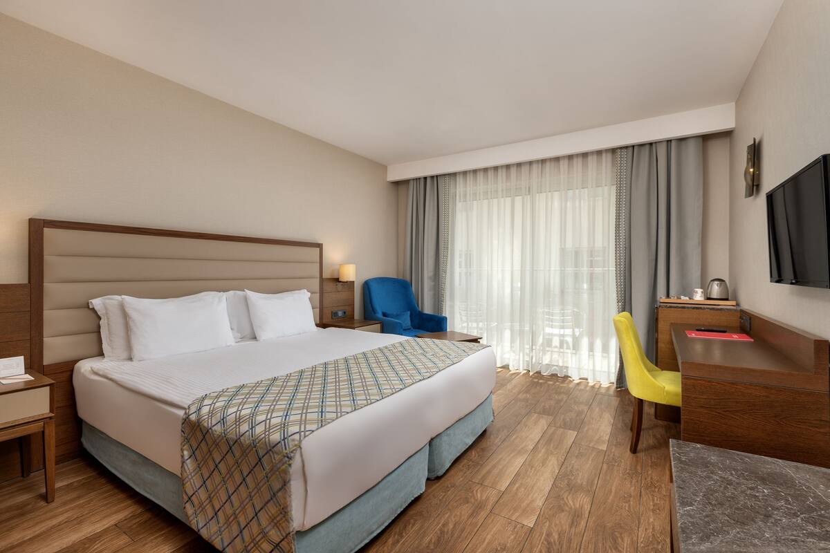Une chambre d’hôtel avec un grand lit, un bureau, une chaise, une télévision et une fenêtre avec des rideaux.