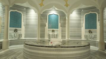 Une salle de spa luxueuse dotée d’une grande baignoire circulaire en marbre, de colonnes blanches et de fenêtres aux carreaux bleus.