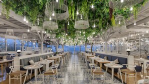 Un restaurante espacioso con techos altos, lámparas colgantes y vistas a la ciudad.