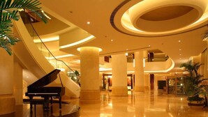 A grand lobby with a grand piano, a curved staircase, and a spacious area with columns and plants. - New Century Grand Hotel Changchun (Changchun)