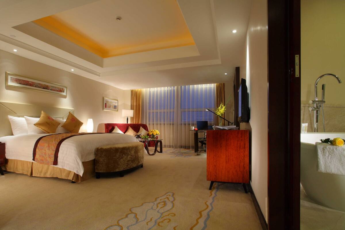 Ein Hotelzimmer mit einem großen Bett, einem Schreibtisch, einem Stuhl, einem Fernseher und einem Badezimmer mit Badewanne und Dusche.