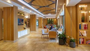 A modern hotel lobby with wooden paneling, a reception desk, seating area, and a bookshelf. - Diamond Hotel (Sunny Beach)
