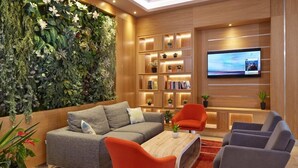 A modern living room with a grey sofa, orange and grey chairs, a wooden coffee table, and a TV mounted on the wall. - Diamond Hotel (Sunny Beach)