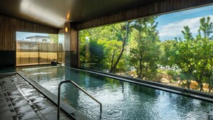 A modern indoor swimming pool with a large window offering a view of lush greenery and a mountain range. - Tokiwa Hotel (Kofu)