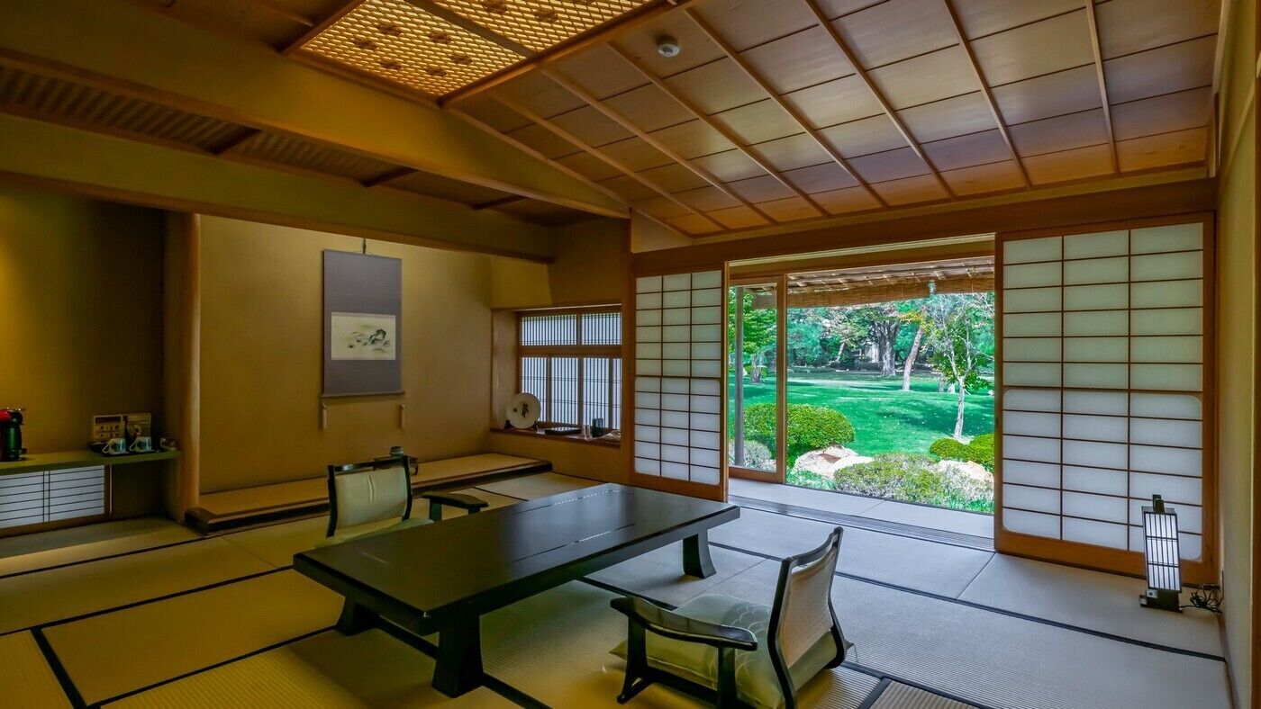 A traditional Japanese room with tatami flooring, a low table, and sliding doors with a view of a garden.