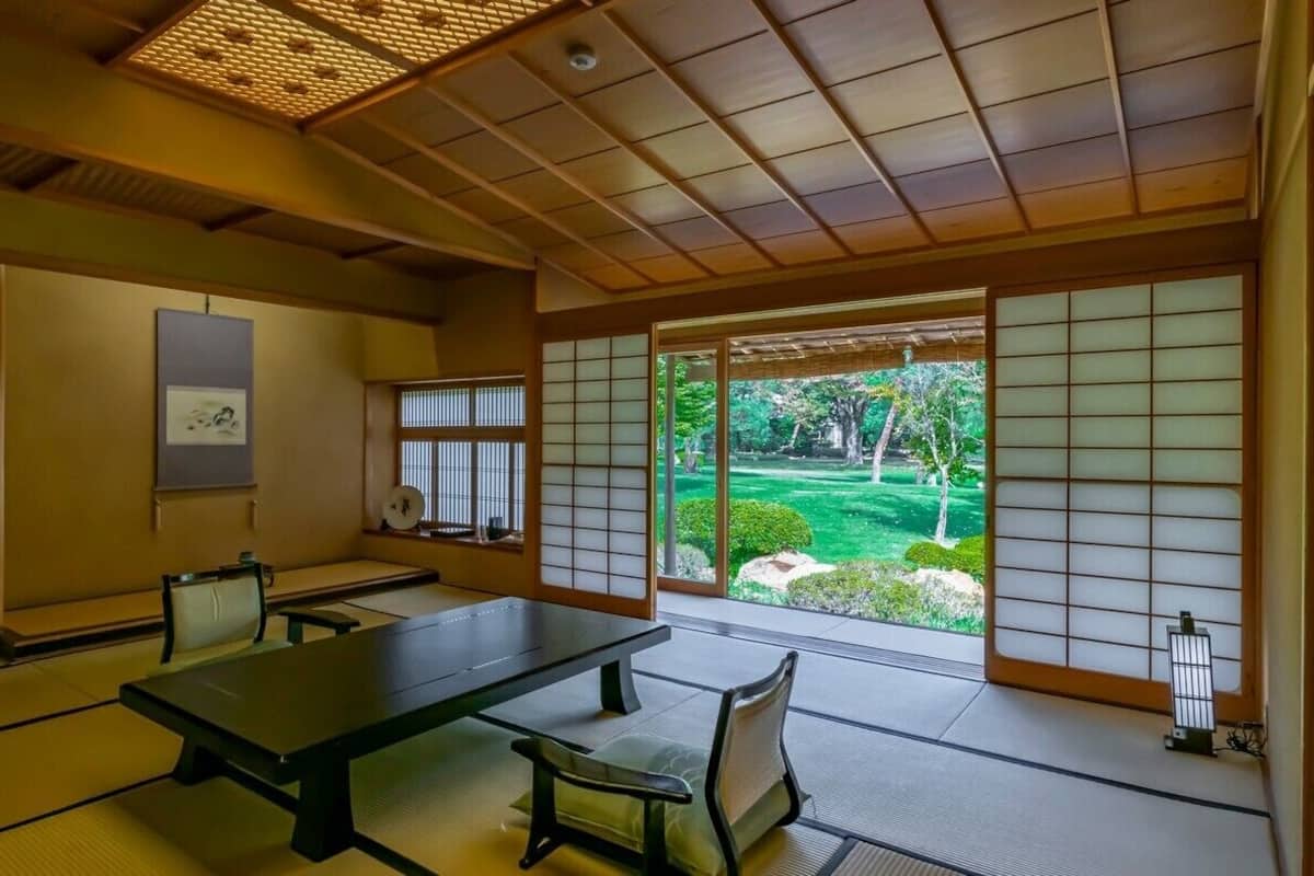 A traditional Japanese room with tatami flooring, a low table, and sliding doors with a view of a garden.
