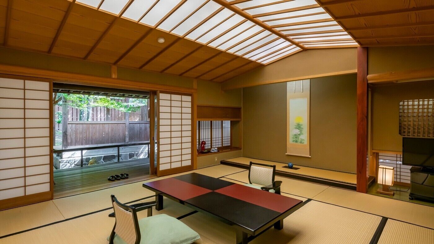 A tatami mat room with a low table, chairs, sliding doors, and a view of the outside.