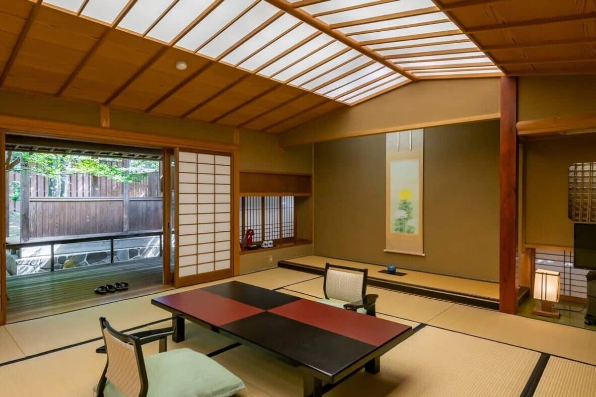 A tatami mat room with a low table, chairs, sliding doors, and a view of the outside.